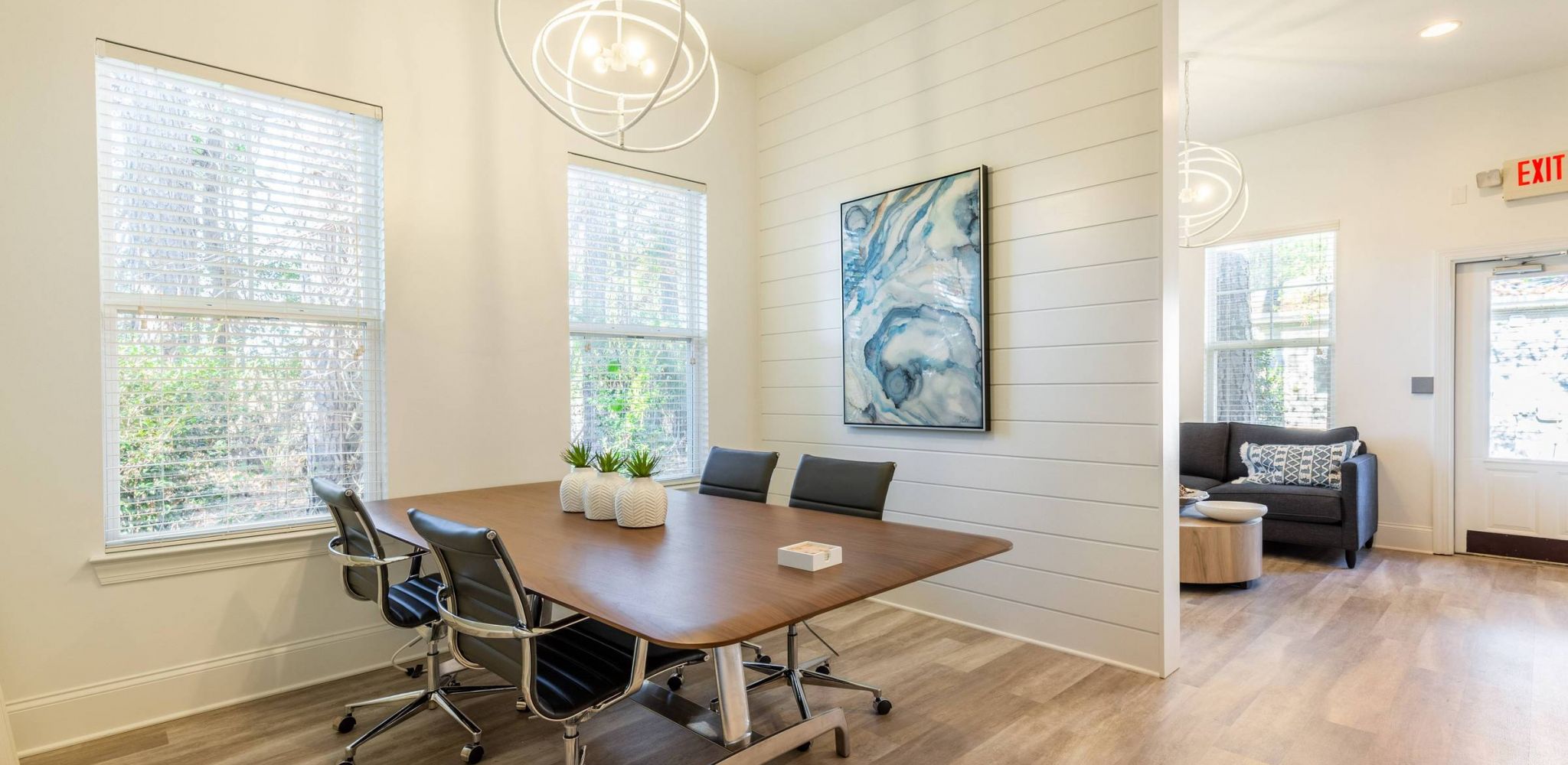 Hawthorne at Murrayville bright meeting room with large windows, a wooden table, black chairs, and abstract wall art