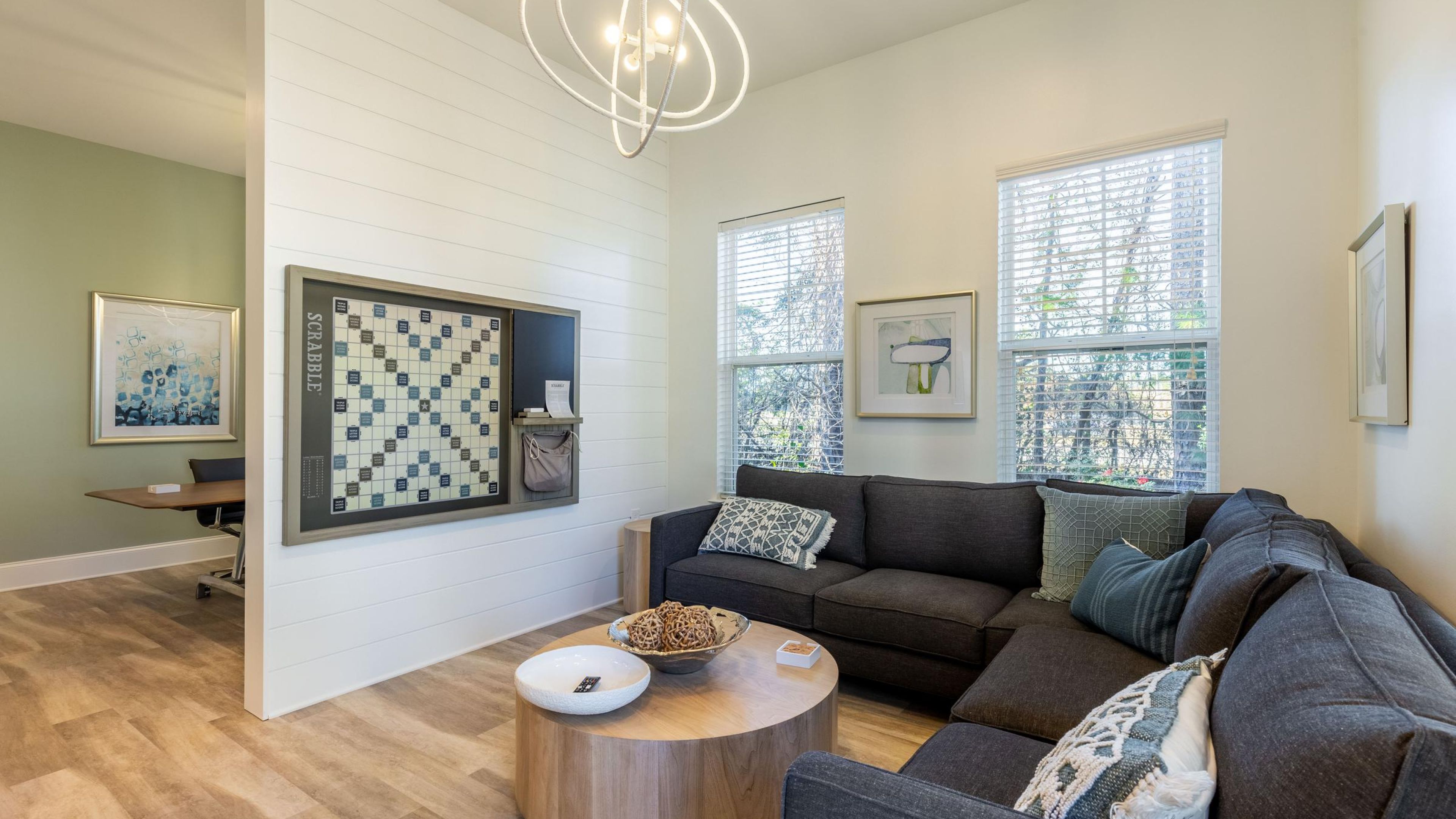 Hawthorne at Murrayville cyber cafe sectional couch with round wooden coffee table and wall game in a room with windows and modern light fixture.