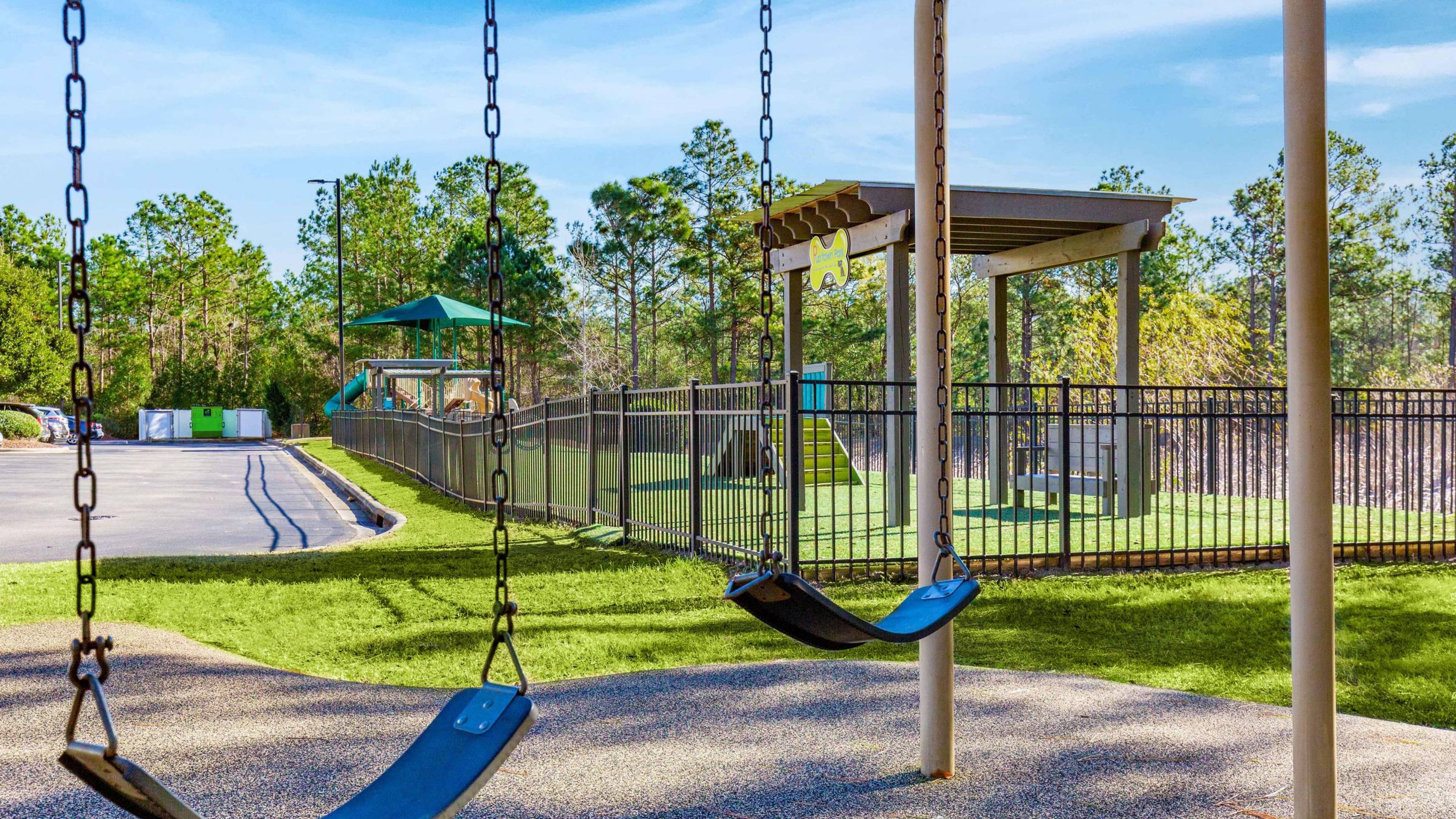 Hawthorne at Murrayville playground with blue swings, green turf, and tall pine trees in a sunny park setting